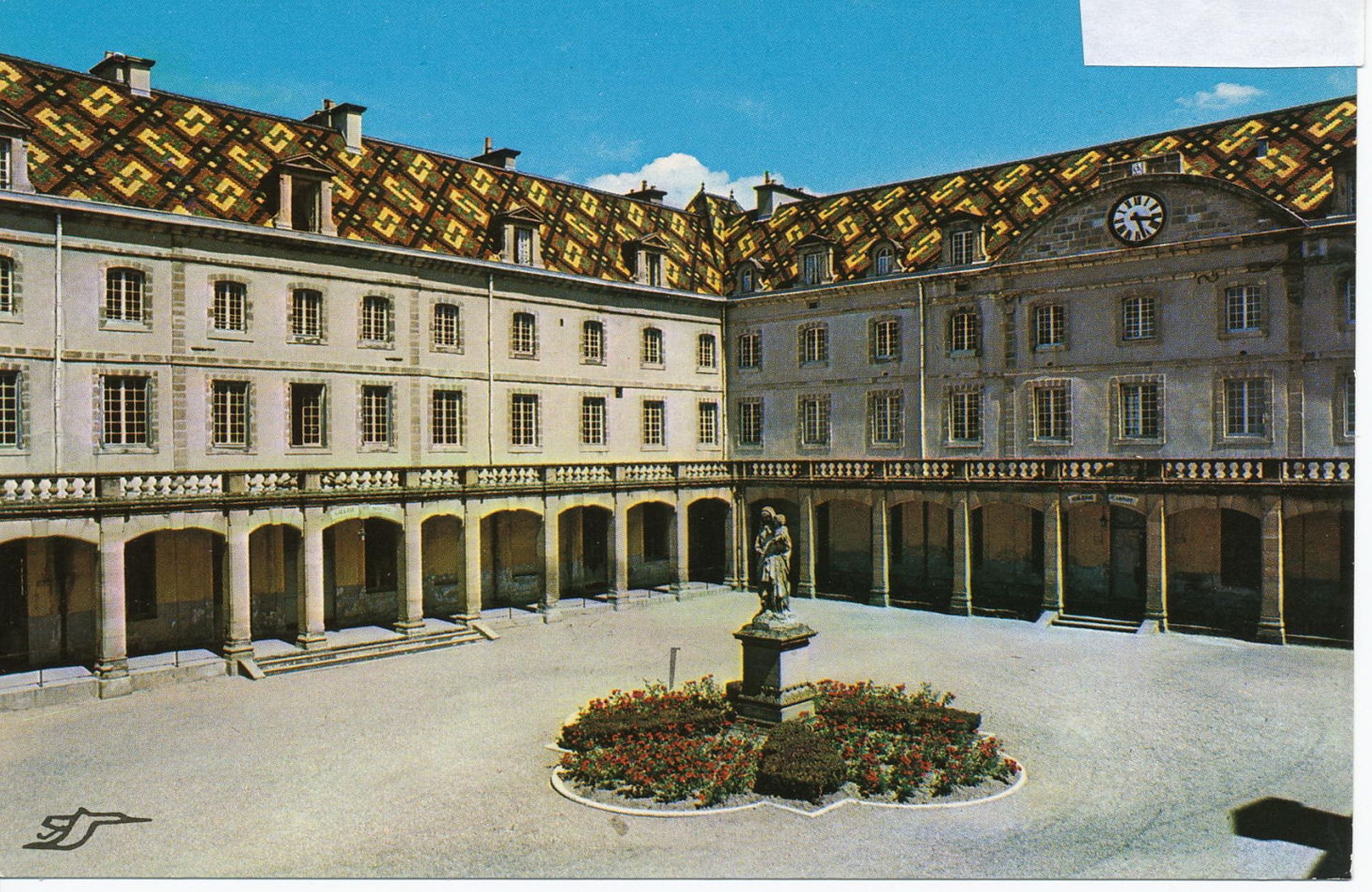 Vue sur la cour intérieure de l'école militaire d'Autun. Au centre, une statue et dans l'angle, des arches surmontées des bâtiments dont la toiture est en ardoises colorées. 